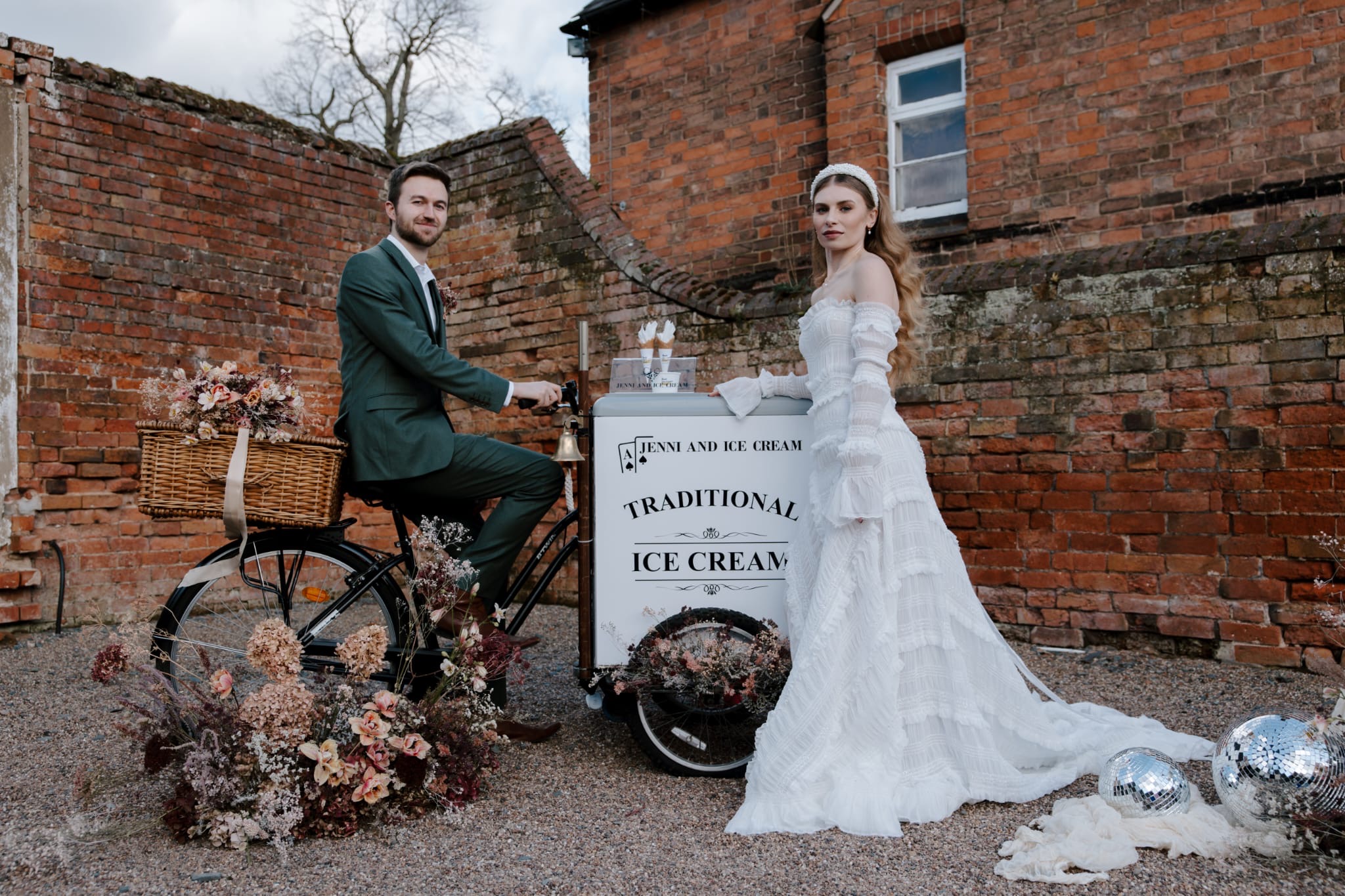 Bride and groom with a black vintage ice cream trike against a brick wall